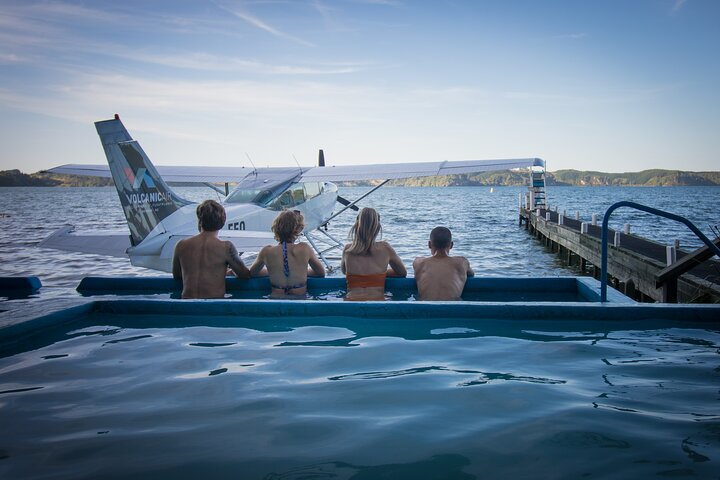 Soak in serene views from a hot pool as you watch floatplanes glide over Lake Rotoiti combining relaxation and adventure in Rotorua's hidden lakes district.